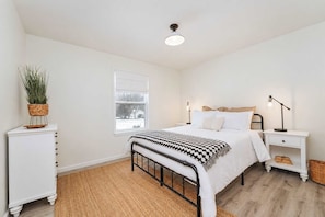 A bedroom with a bed, bedside tables, a lamp, a plant, and a window. - Blue Haven Retreat | Pool • Theater • Arcade Room! (Fennville)