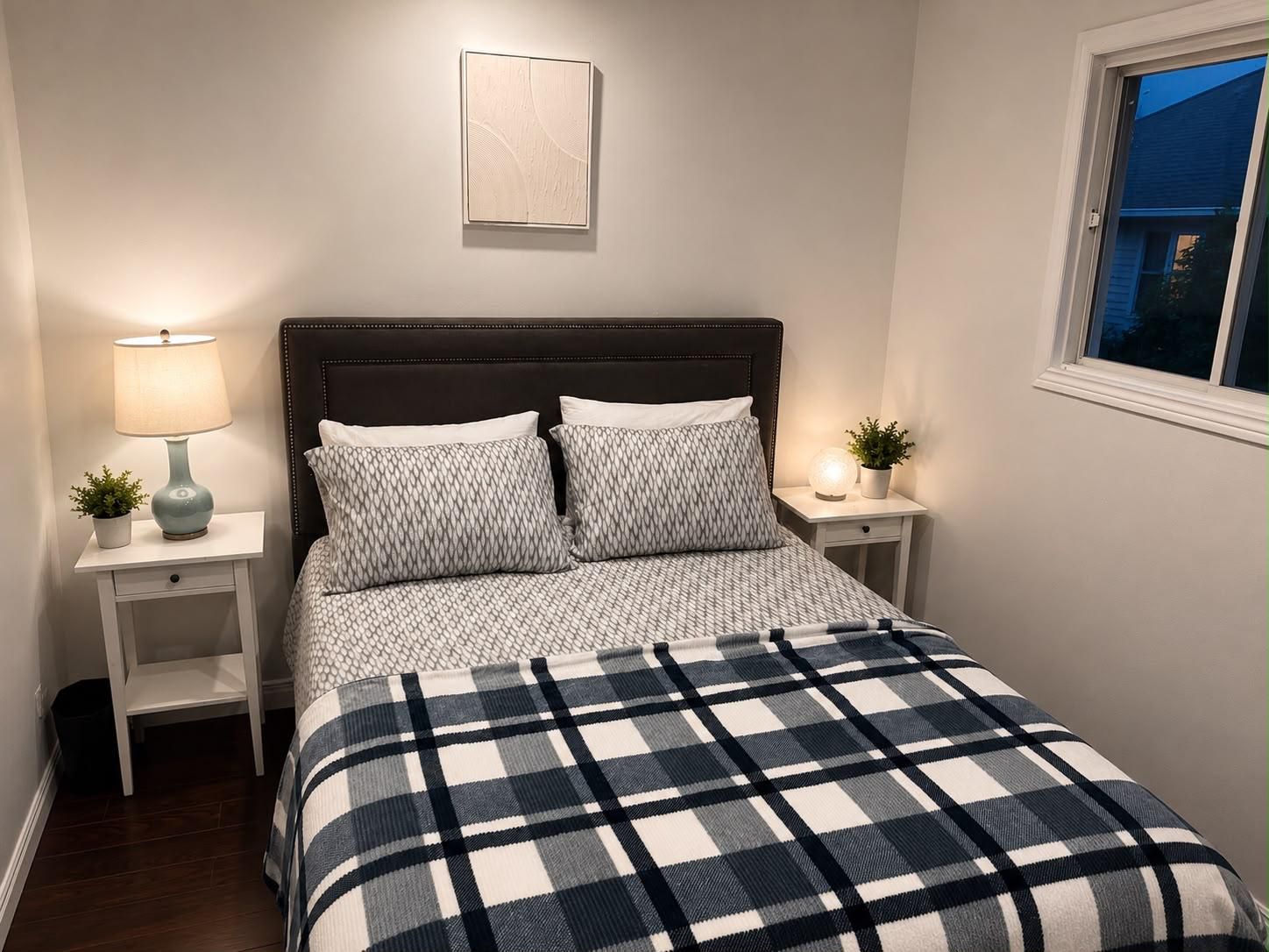 A bedroom with a bed, two bedside tables, a nightstand, a lamp, and a window.