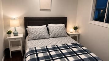 A bedroom with a bed, two bedside tables, a nightstand, a lamp, and a window.
