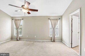 A room with a ceiling fan, two windows with curtains, a door, and a carpeted floor. - jjjjjjjjjjj (Hanover)