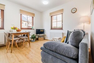 Una sala de estar acogedora con un sofá gris, una mesa de comedor de madera con sillas, un televisor y un ventanal con vistas.