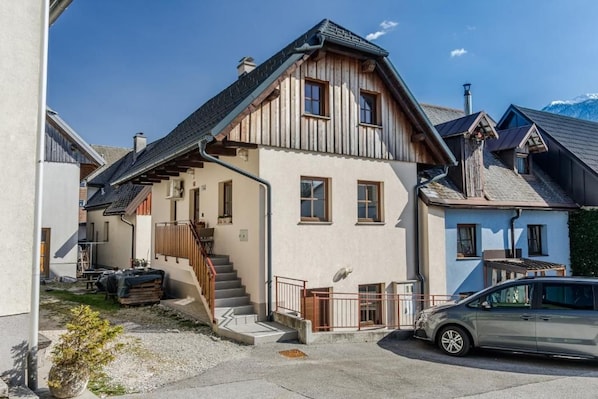 Une maison à deux étages avec une façade en bois, un escalier apparent et une voiture garée.