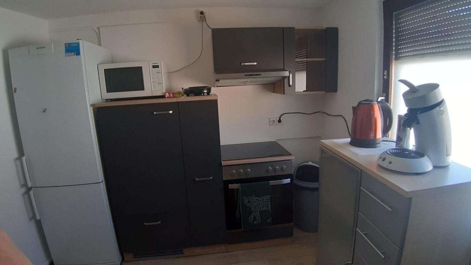 Eine kompakte Küche mit Kühlschrank, Mikrowelle, Herd, Backofen und Kaffeemaschine.