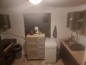 Una kitchenette compacta con cafetera, microondas y un refrigerador pequeño. Hay un cesto de basura y un armario de madera a la izquierda.
