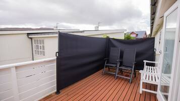 Un balcone con pavimento in legno, un pannello privacy nero e due sedie.