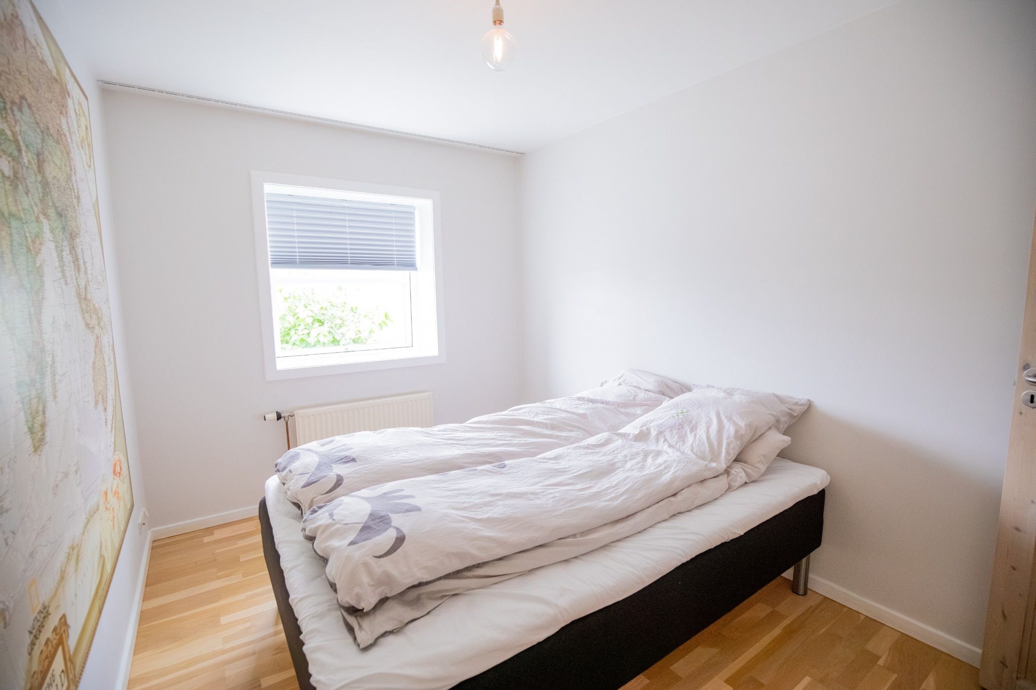 Une chambre avec un lit simple, une fenêtre avec des stores et un radiateur.