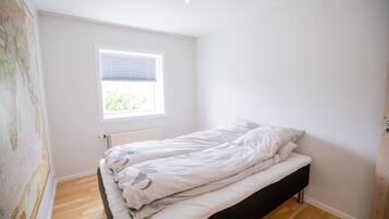 Une chambre avec un lit simple, une fenêtre avec des stores et un radiateur.