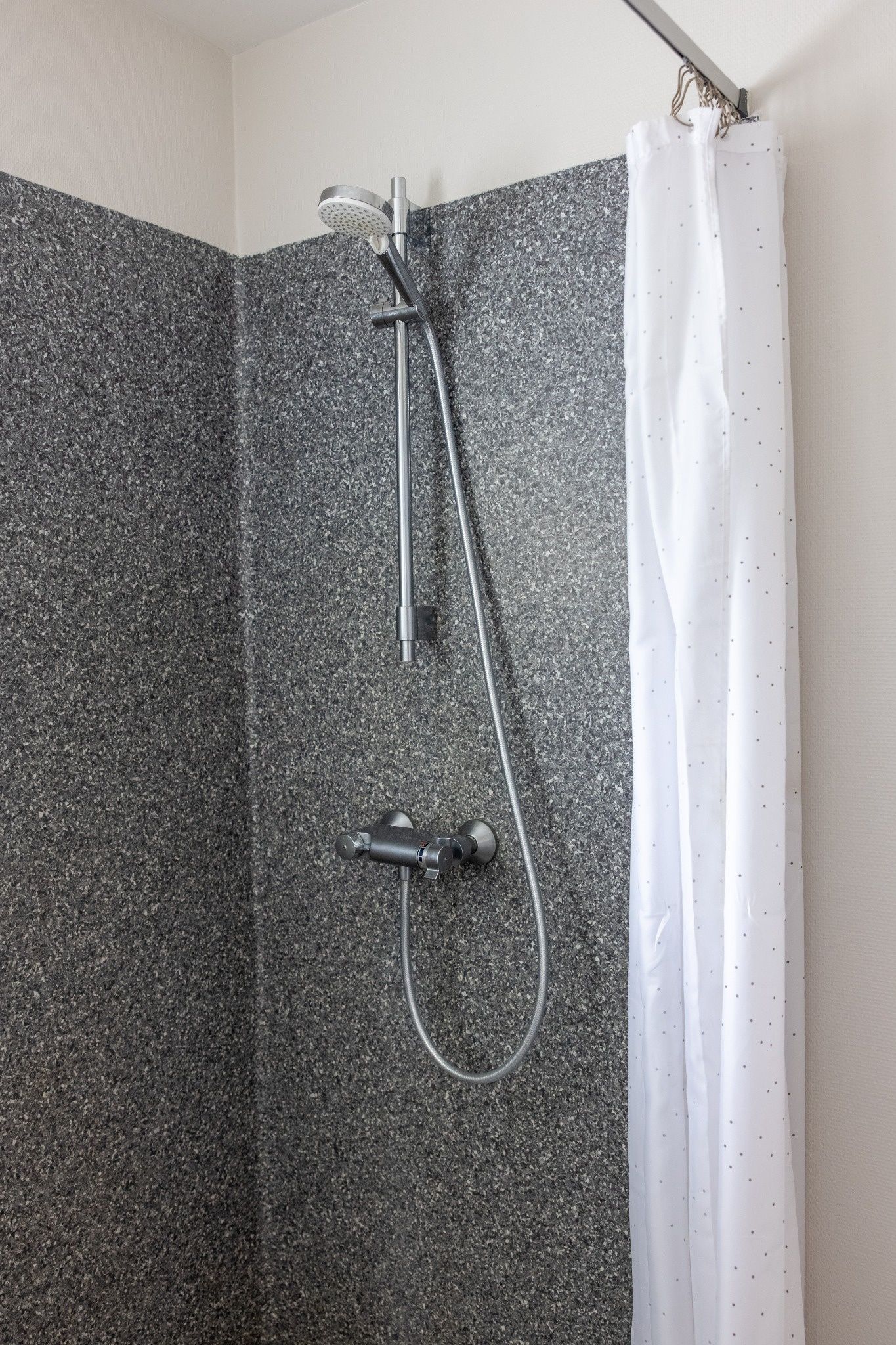 Ducha con cabezal de ducha manual y grifo empotrado en una pared moteada.
