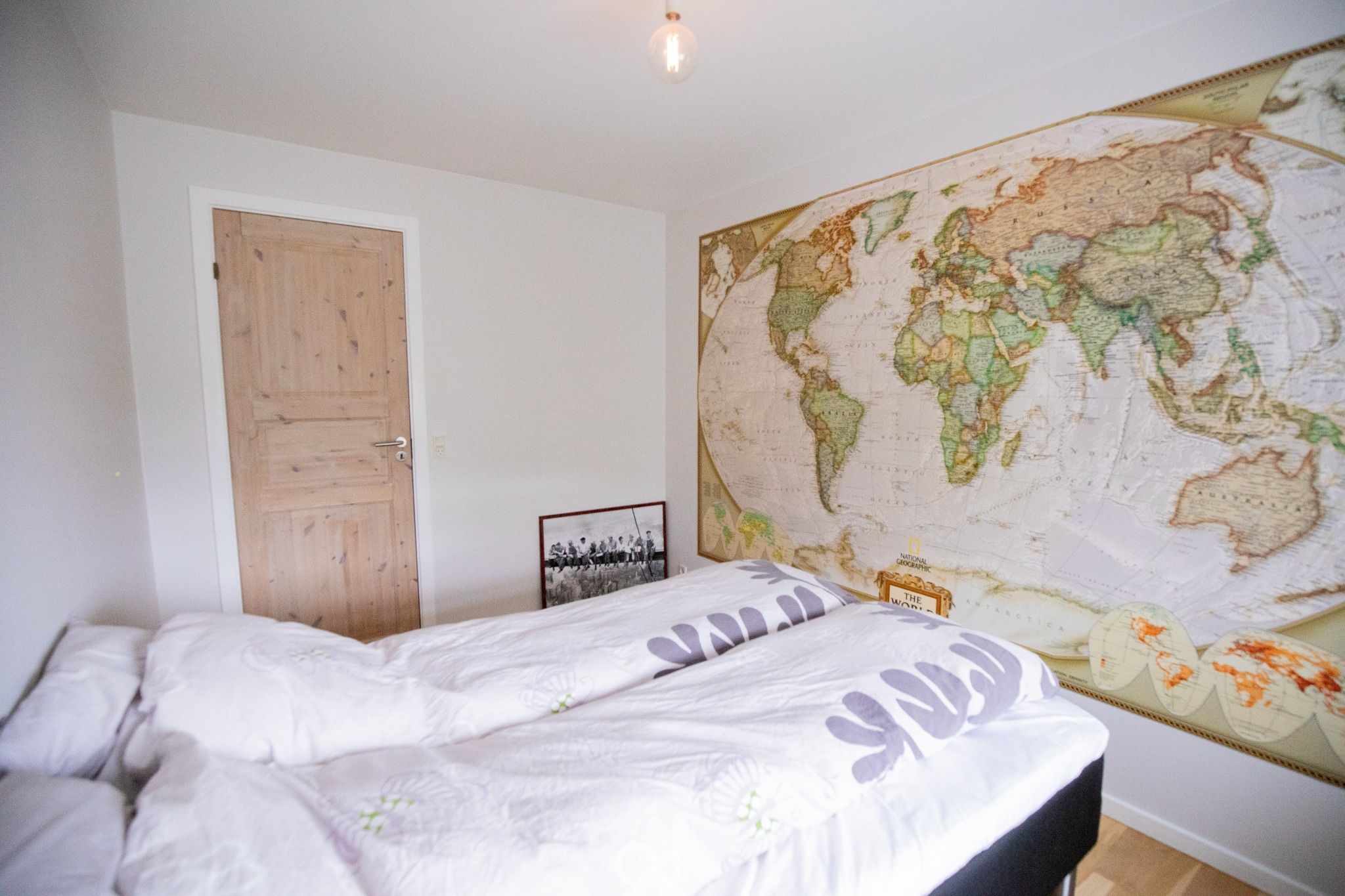 Een slaapkamer met een bed, een houten deur en een grote wereldkaart aan de muur.