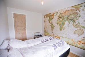 A bedroom with a bed, a wooden door, and a large world map on the wall. - Heinagerði 10A (Thorshavn)