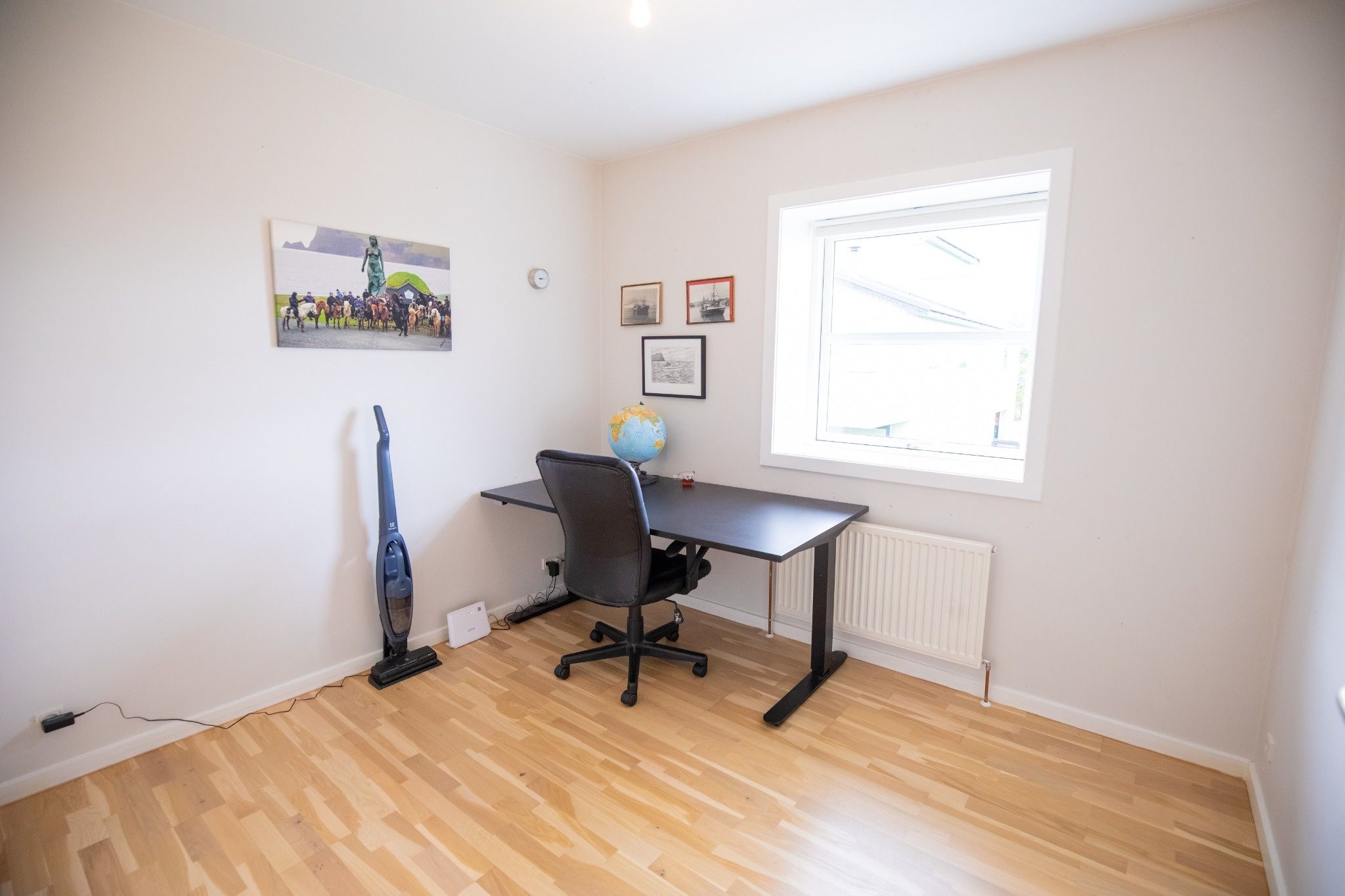 Una habitación con piso de madera, un escritorio con silla, un globo terráqueo y una ventana con persianas.