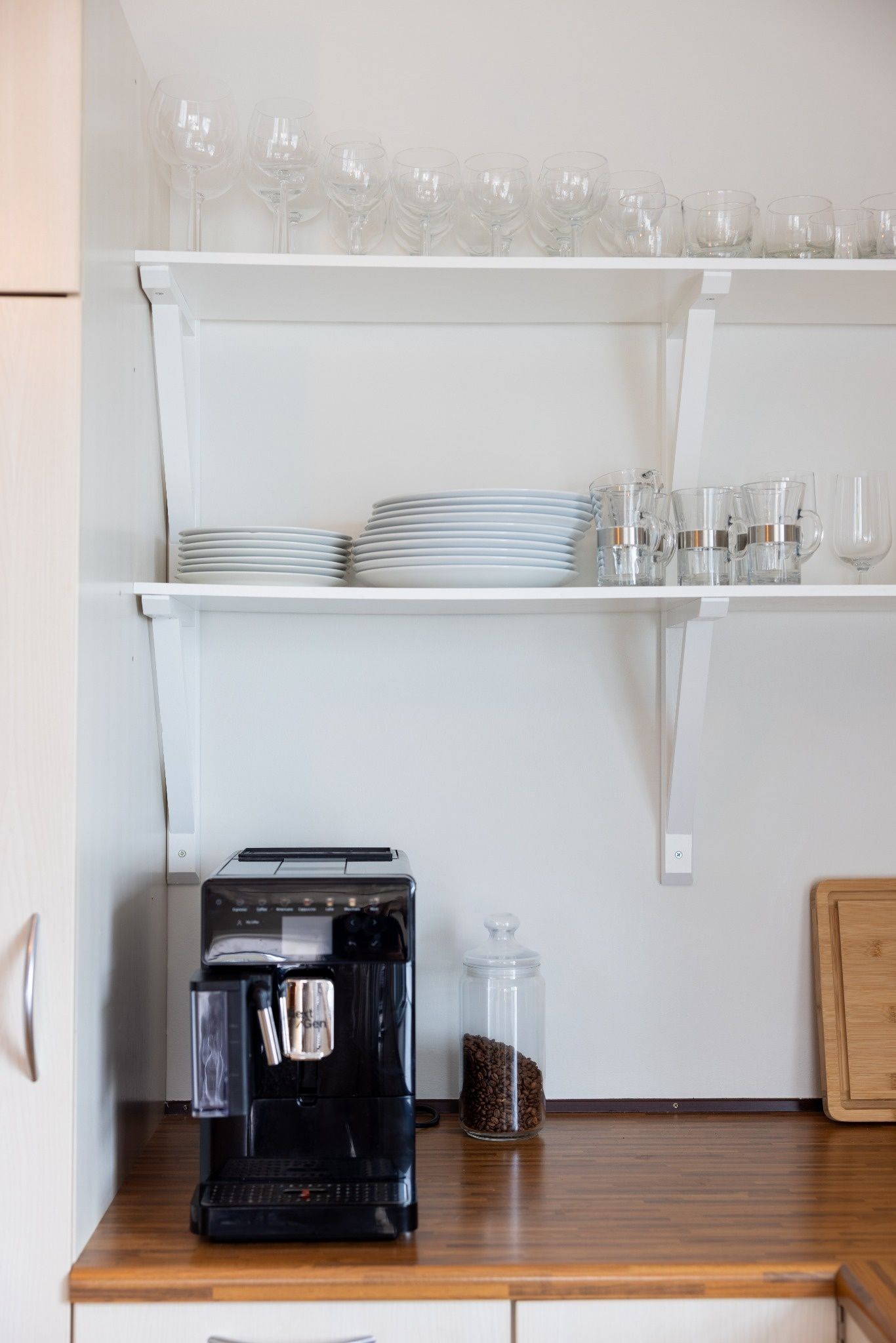 Een keuken met een koffiezetapparaat, een pot koffiebonen, en planken met drinkglazen en borden.