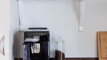 Een keuken met een koffiezetapparaat, een pot koffiebonen, en planken met drinkglazen en borden.