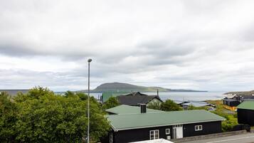 A coastal village with houses, a street lamp, and a view of the sea and hills.