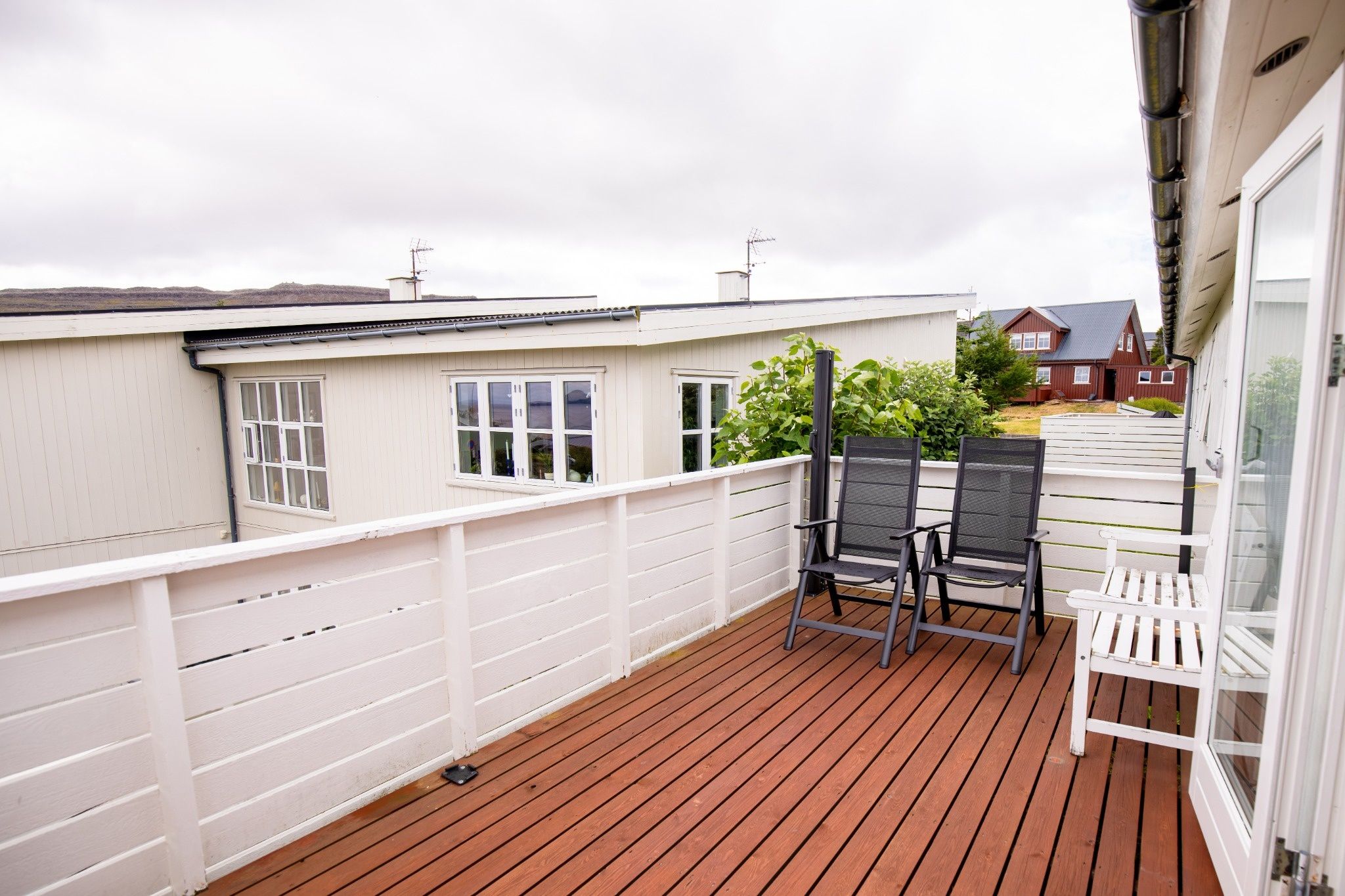 Een houten terras met twee stoelen en een witte leuning.