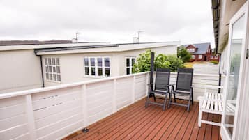 Een houten terras met twee stoelen en een witte leuning.