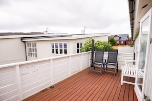 A wooden deck with two chairs and a white railing. - Heinagerði 10A (Thorshavn)