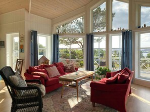A spacious room with large windows, a red sofa, a wicker chair, and a wooden table. - Cabin near Tveitafossen and Fitjarfjellet (Fitjar)
