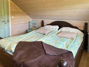 A bedroom with a wooden ceiling, a bed with patterned bedding, a nightstand, and a door. - Cabin near Tveitafossen and Fitjarfjellet (Fitjar)