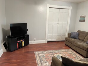 A living room with a flat-screen TV on a stand, a brown sofa, a patterned rug, and a white door with a decorative frame. - Spacious 7-bedroom house in serene Fort Wayne with AC. Big Groups only (Fort Wayne)