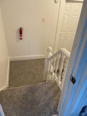 A staircase with a white balustrade and a fire extinguisher mounted on the wall. - Spacious 7-bedroom house in serene Fort Wayne with AC. Big Groups only (Fort Wayne)