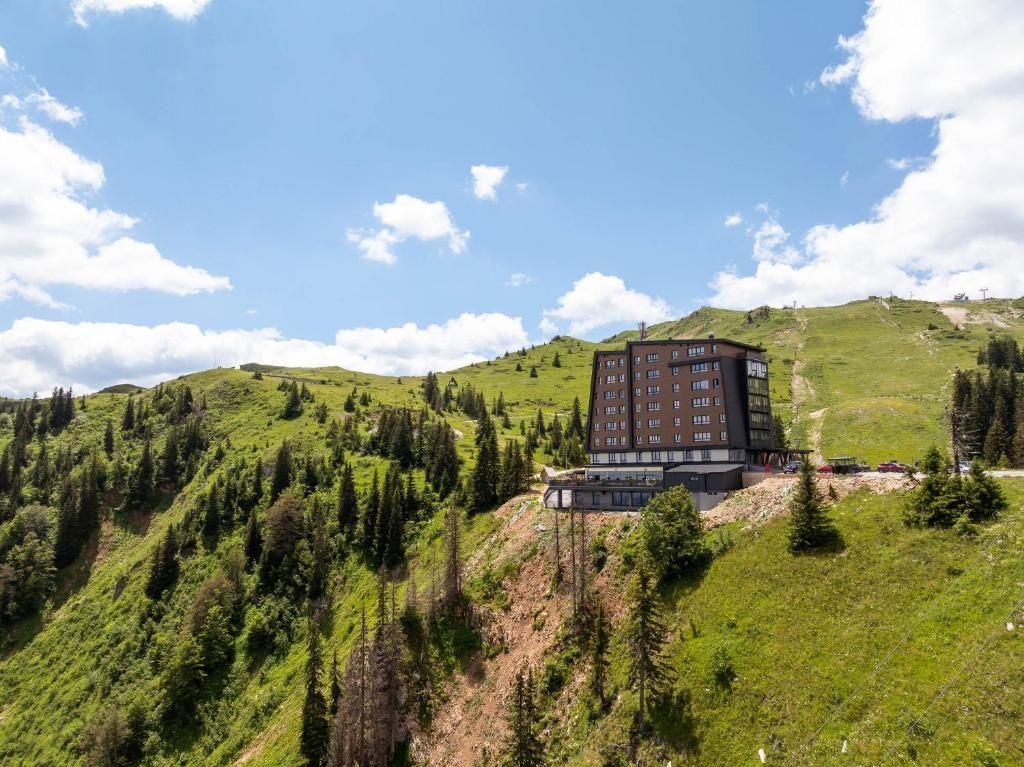 Ein modernes Gebäude mit Flachdach, umgeben von einer gebirgigen Landschaft mit dichten Wäldern.
