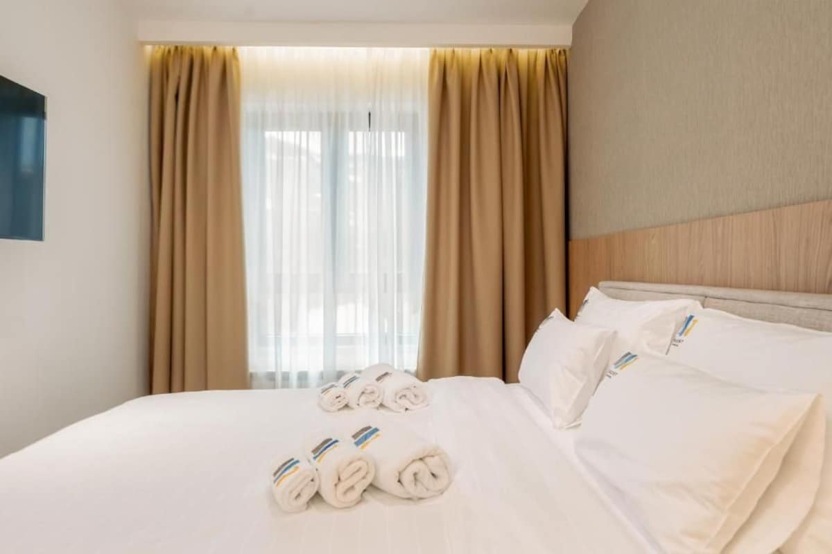 Ein Hotelzimmer mit einem Bett, beigen Vorhängen und zusammengerollten Handtüchern.