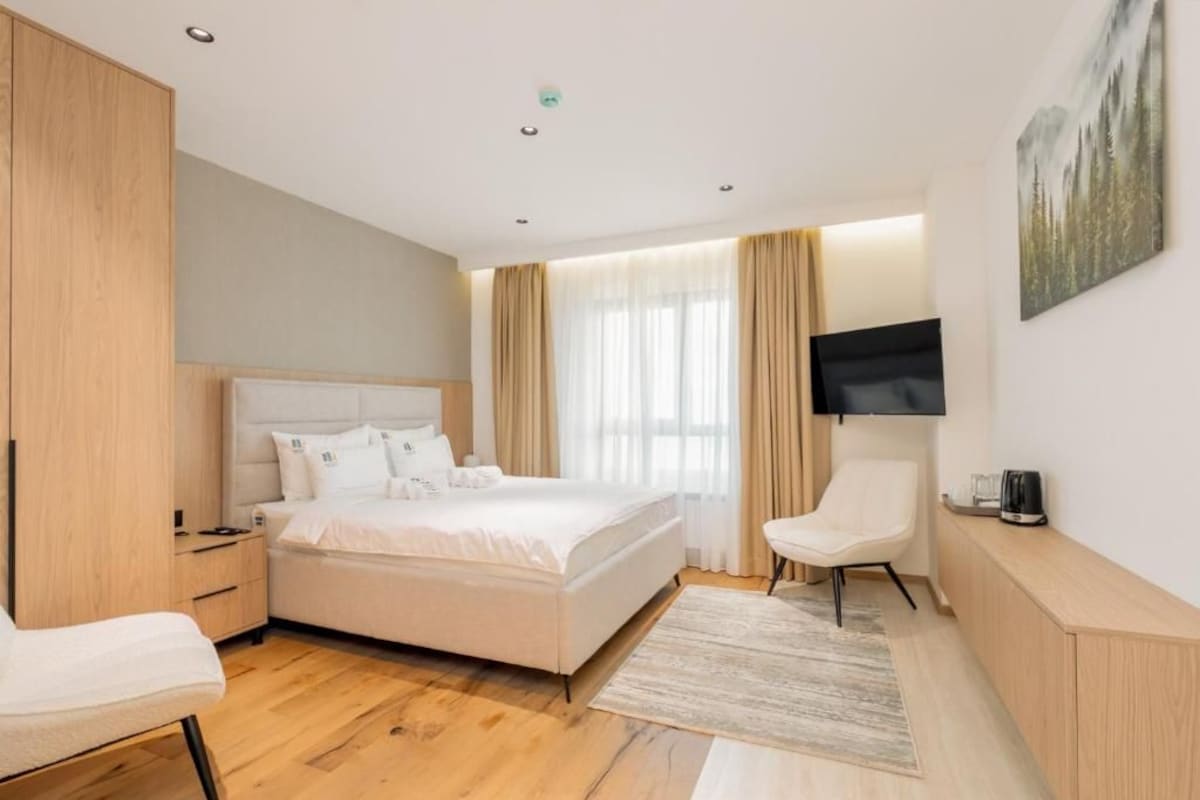 Ein modernes Schlafzimmer mit einem großen Bett, einem Fernseher, einem Sessel und einem Kleiderschrank.