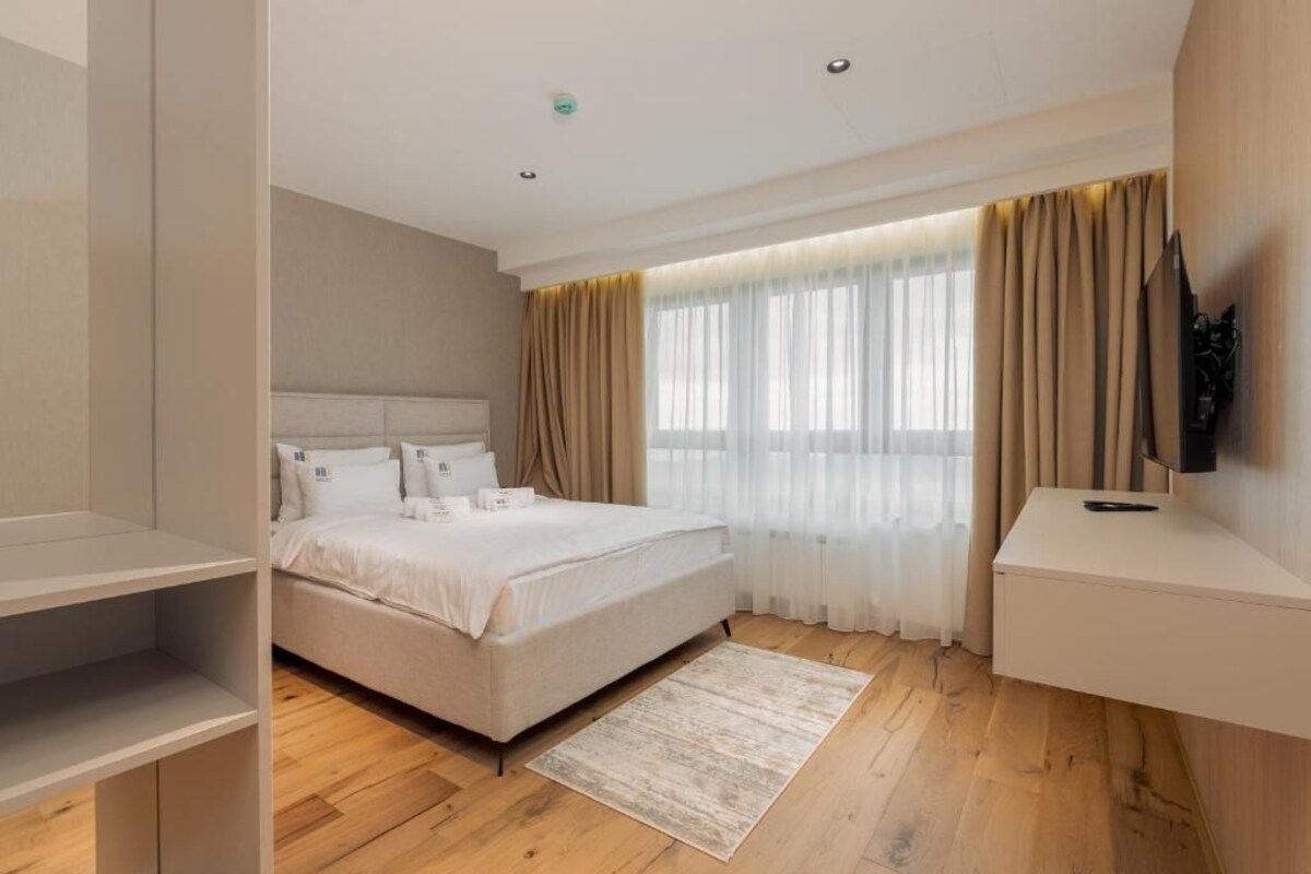 Ein Hotelzimmer mit Bett, Fernseher, Schreibtisch und einem Fenster mit Vorhängen.