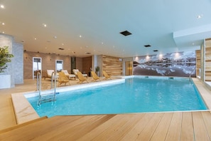 Ein Innenpool mit Holzterrasse, Liegestühlen und einem Wandbild eines Sees.