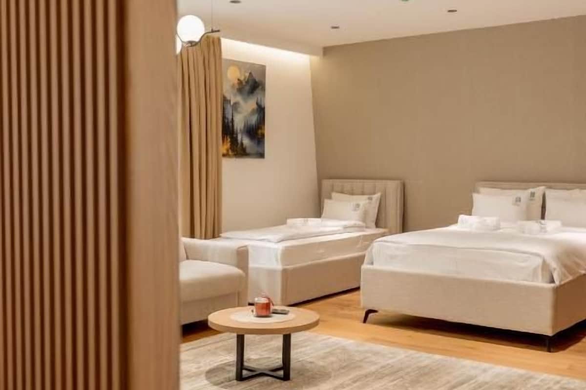Ein modernes Hotelzimmer mit einem Bett, zwei Sofas, einem kleinen runden Tisch und einem Holzakzent.