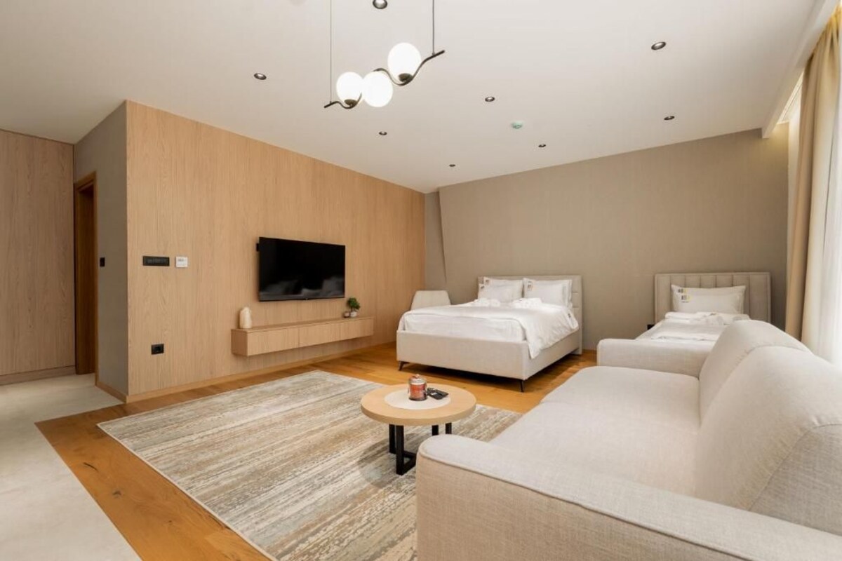 Ein modernes Schlafzimmer mit einem großen Bett, einer Couch, einem an der Wand befestigten Fernseher und einem kleinen Tisch.