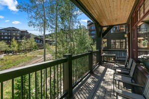 Eine Holzterrasse mit Sitzgelegenheiten im Freien, mit Blick auf ein Wohngebiet mit mehreren Gebäuden und Bäumen.