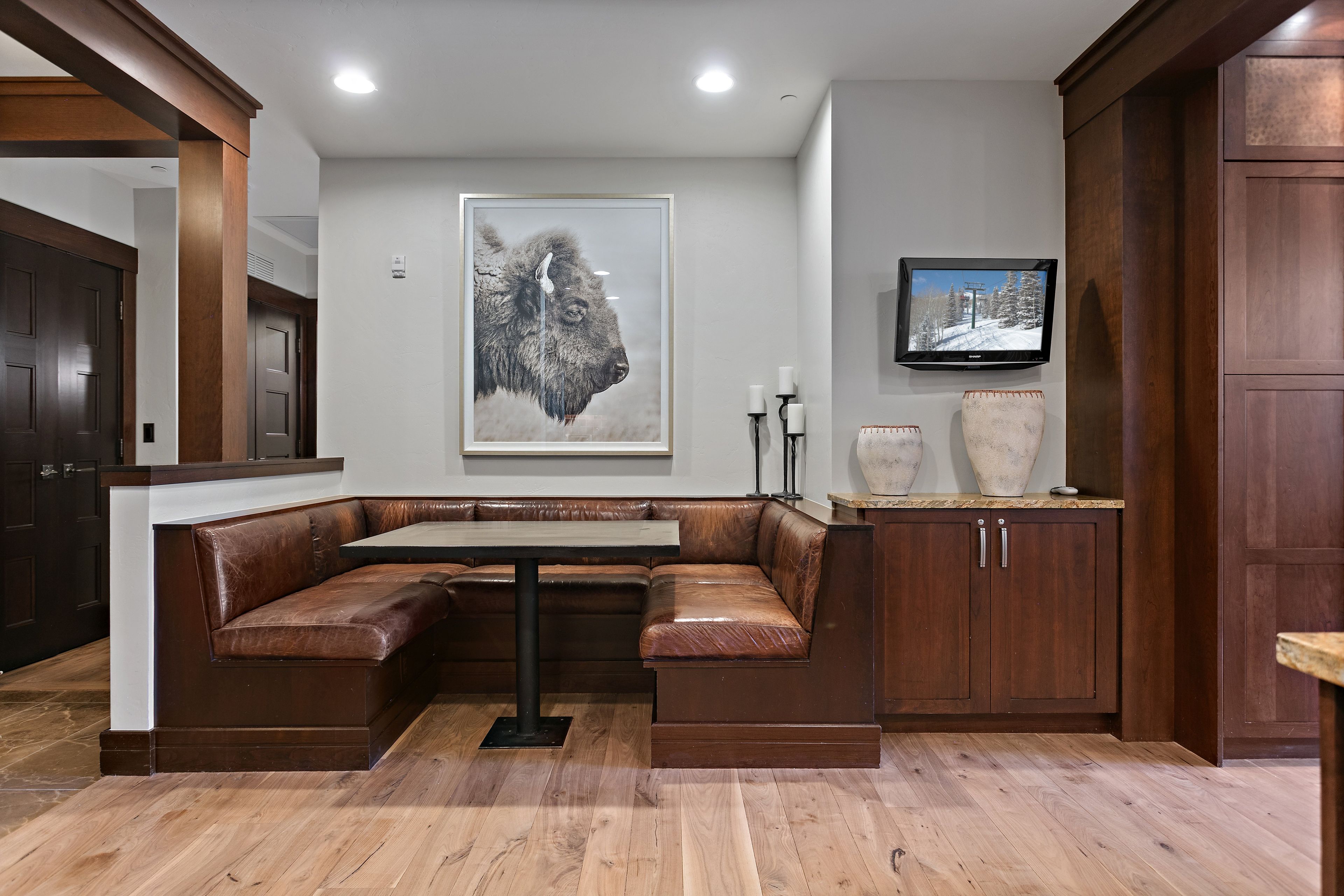 A modern interior with a wooden bench seating area, a flat-screen TV mounted on the wall, and a large framed artwork above the bench.