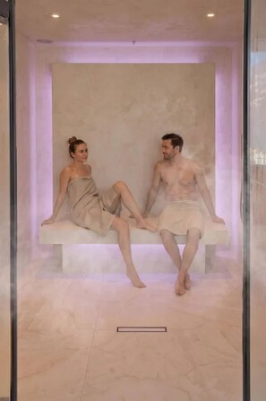 Two people sitting on a bench in a room with a marble floor and a plain wall. - Luxury Accommodation on 200m2 With Private spa (Beckenried)