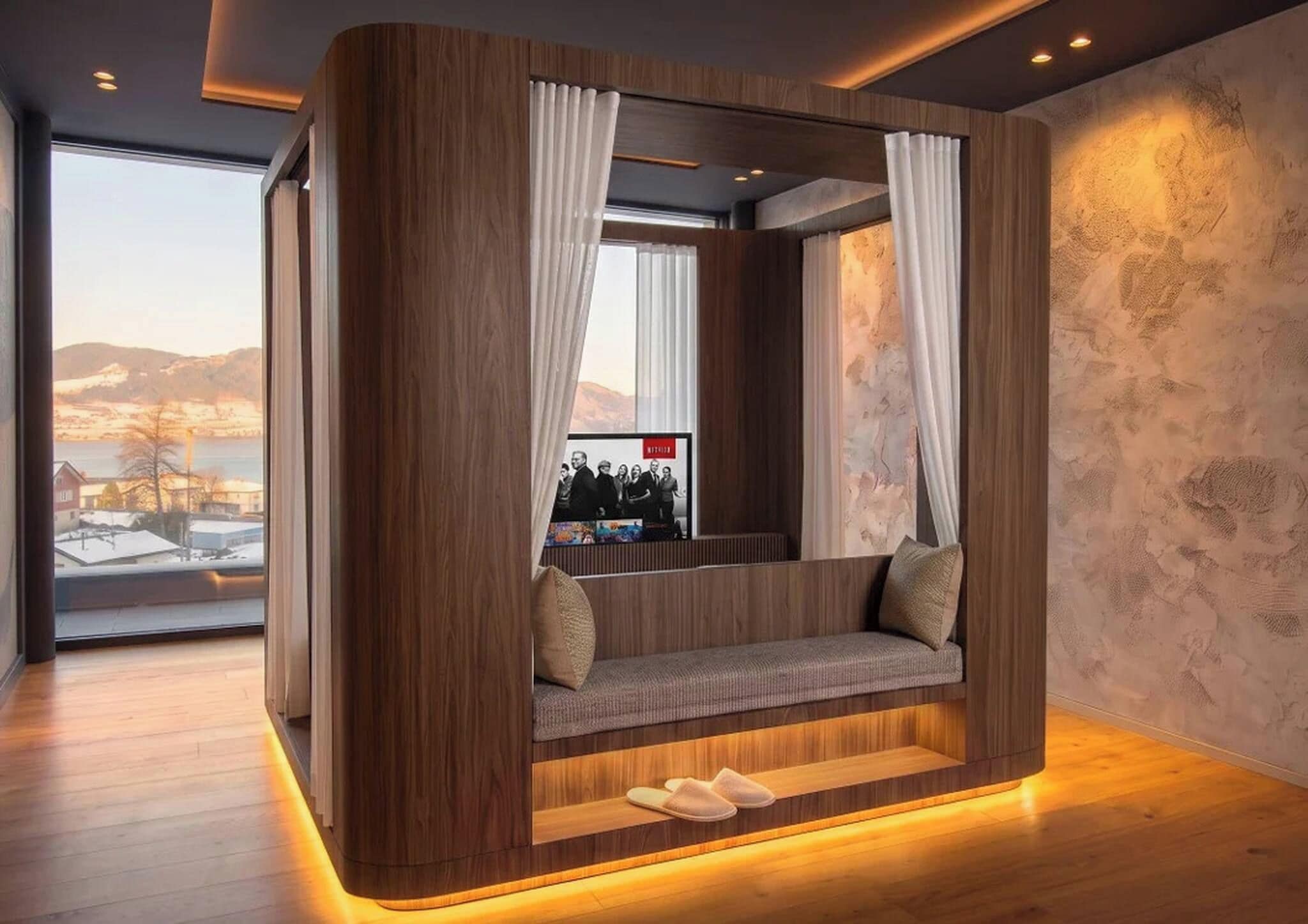 A modern room with a wooden accent wall, a cushioned bench with pillows, and a view of a cityscape through a window.
