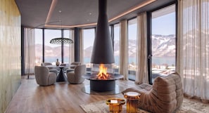 A modern living room with a fireplace, large windows, and a view of mountains. - Luxury Accommodation on 200m2 With Private spa (Beckenried)