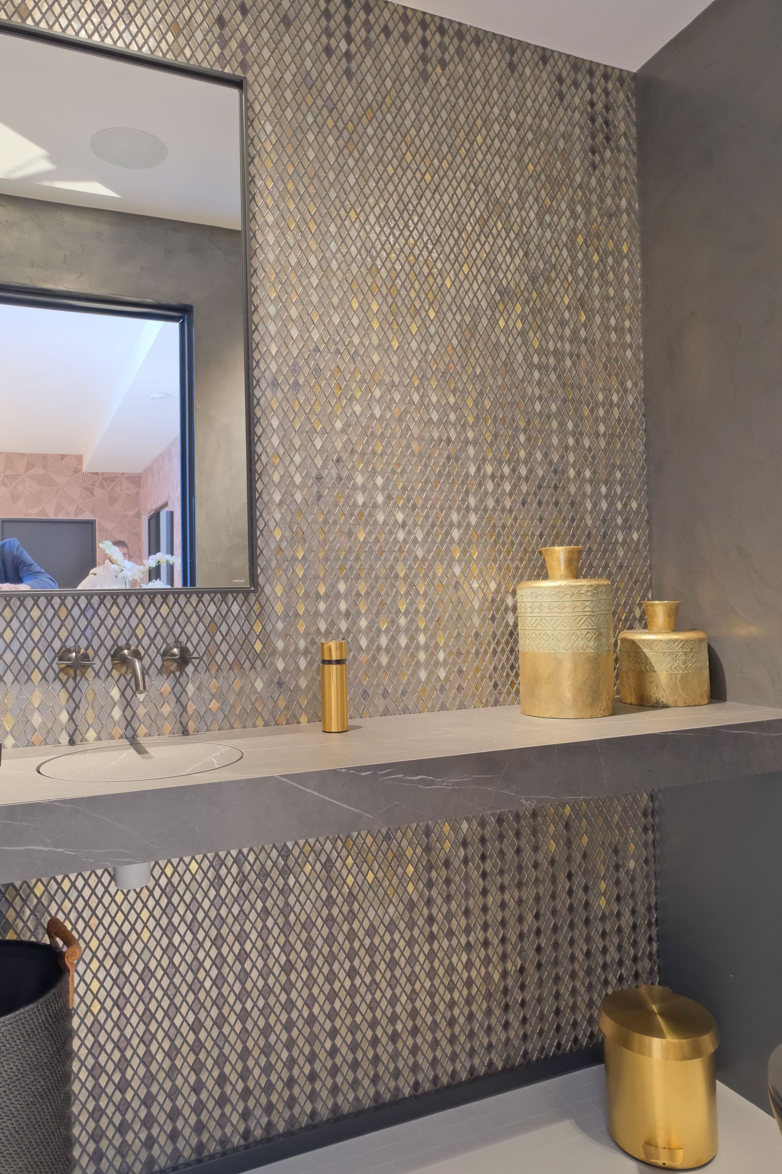 A bathroom with a modern sink, a mirror, and decorative golden containers.