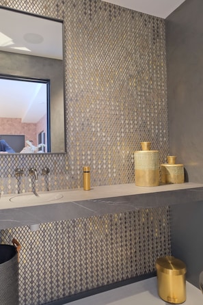 Une salle de bain dotée d’un lavabo moderne, d’un miroir et de jolis récipients décoratifs dorés.