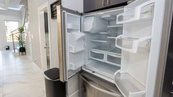 Uma cozinha moderna com geladeira de aço inoxidável, forno embutido e lixeira.