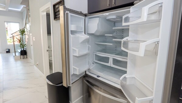 Uma cozinha moderna com geladeira de aço inoxidável, forno embutido e lixeira.