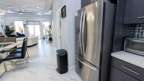 Cozinha moderna com geladeira de aço inoxidável, forno embutido e área de jantar com mesa e cadeiras de vidro.