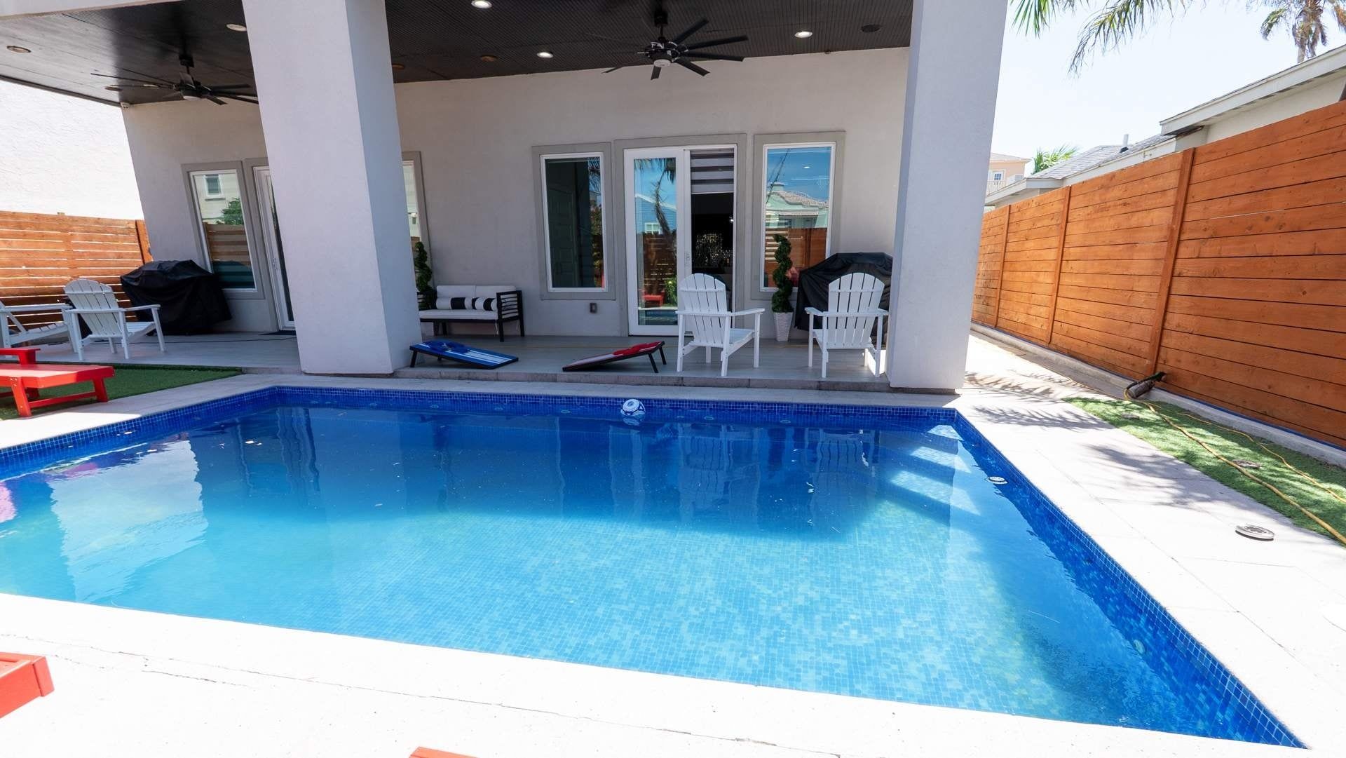 Una piscina con un patio coperto, mobili da esterno e un recinto in legno.