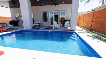Una piscina con un patio coperto, mobili da esterno e un recinto in legno.