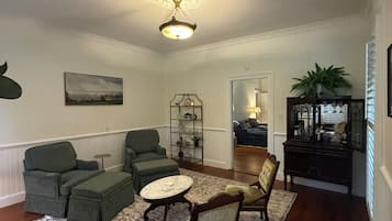 Ett vardagsrum med en mönstrad matta, två gröna fåtöljer, en trästol, ett litet runt bord och en dekorativ taklampa.