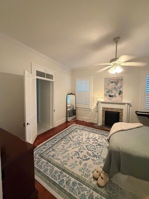 A bedroom with a bed, a fireplace, a ceiling fan, and a door leading to another room. - Historic 4BR Downtown Gem (Greenville)