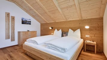 Makuuhuoneessa on puinen katto, valkoisilla lakanoiden peitetty sänky, puinen lipasto ja yöpöytä, jossa on lamppu.