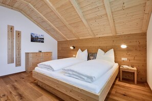 Ein Schlafzimmer mit Holzbalkendecke, einem Bett mit weißen Leinen, einem Holzschrank und einem Nachttisch mit Lampe.