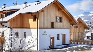 Eine Holzhütte mit geneigtem Dach, einem sichtbaren Eingang und einem Berg im Hintergrund.