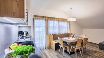 Eine moderne Küche mit eingebautem Geschirrspüler, einem Essbereich mit Holztisch und -stühlen sowie einem Fenster mit durchsichtigen Vorhängen.